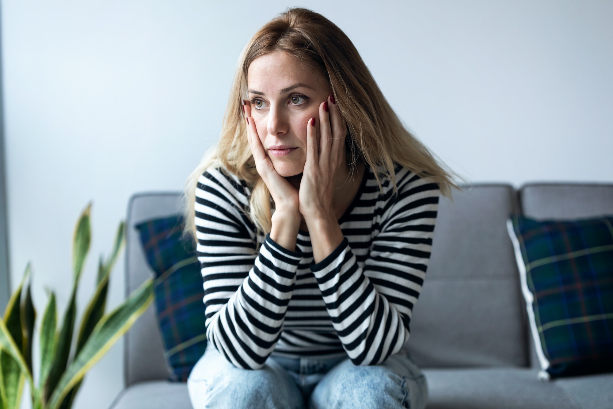 Depressed young woman thinking about her problems while sitting on the sofa at home.