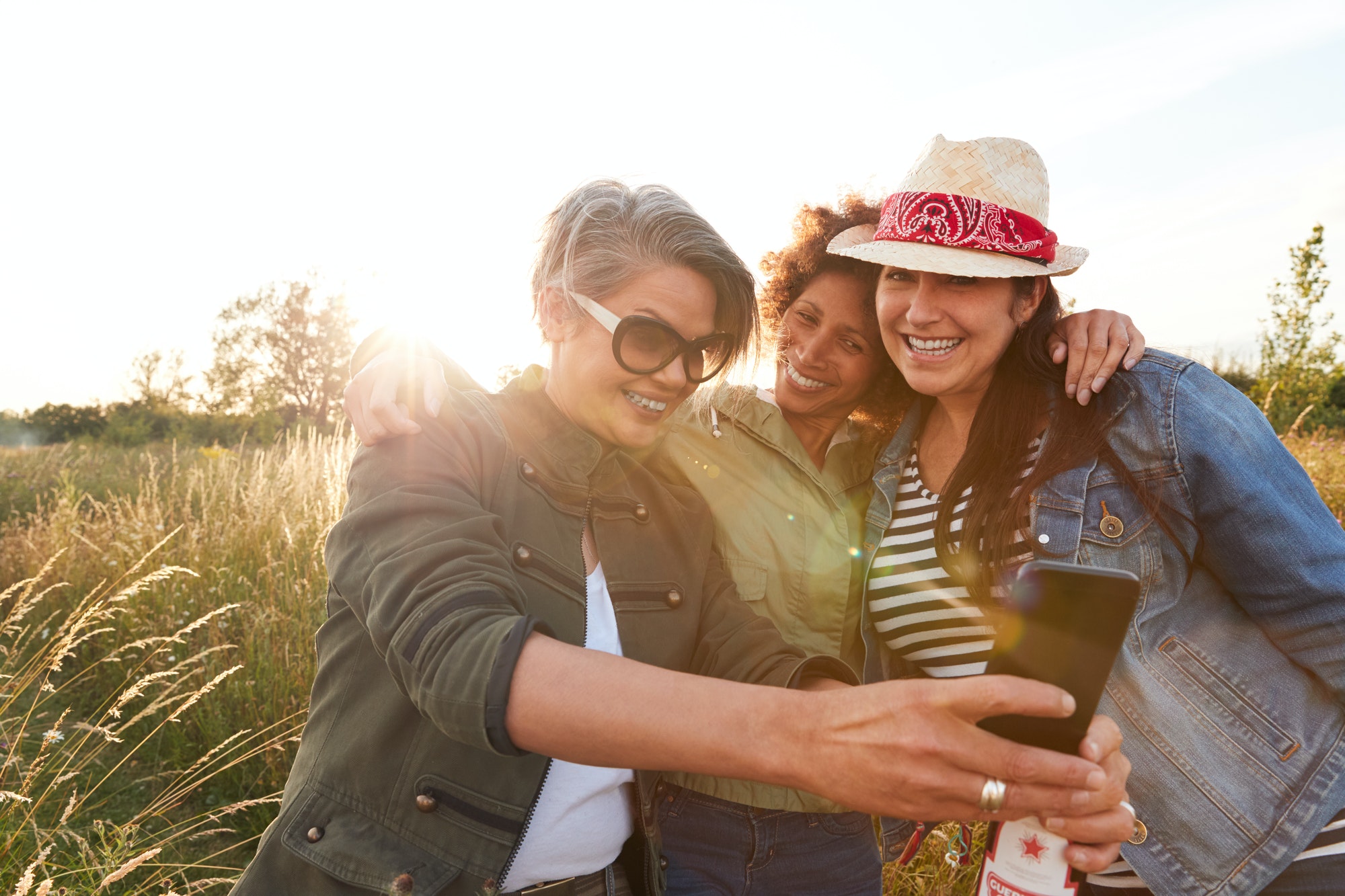 Group Of Mature Female Friends Walking Through Field On Camping Posing For Selfie