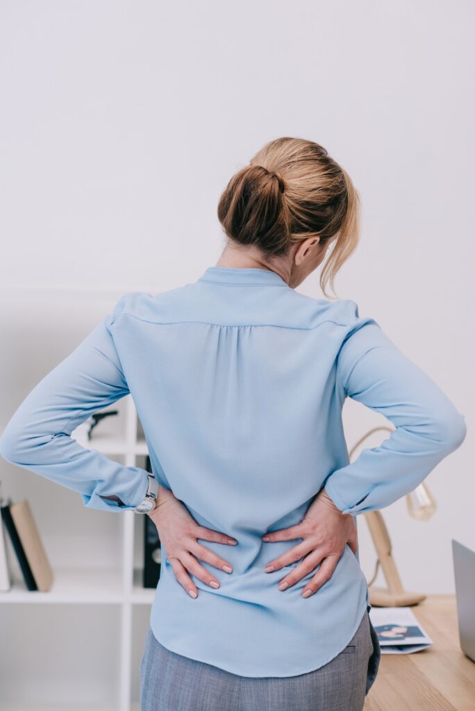 rear view of overworked businesswoman with backpain leaning on table at office