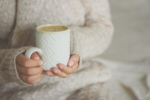 Famale hands holding a cozy ceramic handmade mug with coffe. Winter and Christmas home time concept