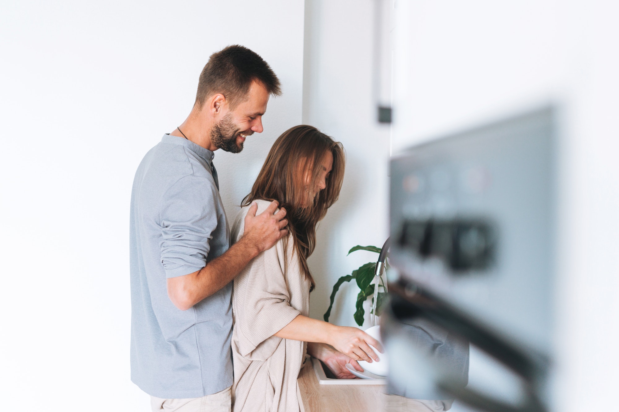 Happy young family couple in love washes dishes in bright modern kitchen