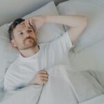 Young tired bearded man lying on bed with open eyes