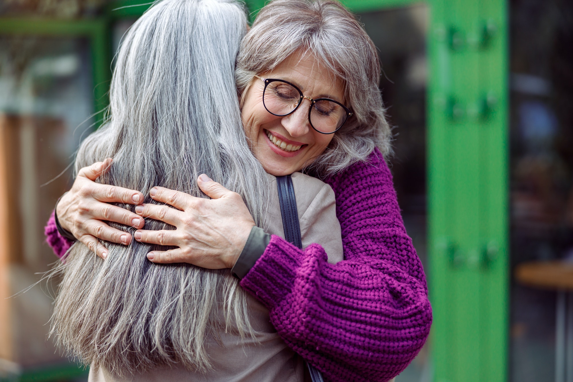 Smiling mature woman embraces female friend meeting on modern city street