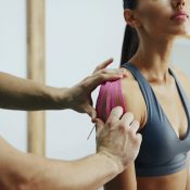 Doctor helps woman by shoulder treatment with kinesio tape