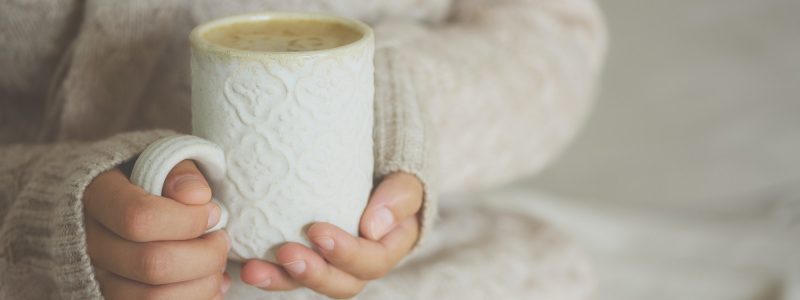 Famale hands holding a cozy ceramic handmade mug with coffe. Winter and Christmas home time concept
