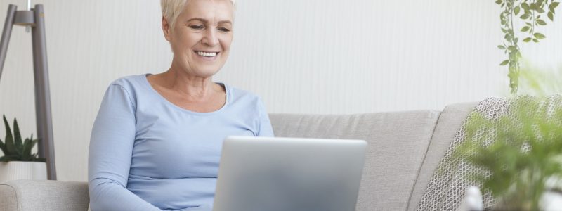 Smiling old woman typing email on laptop