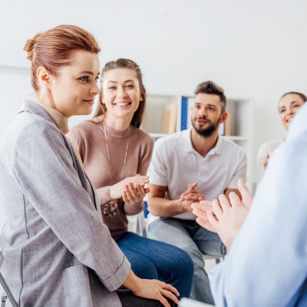 smiling people sitting and applauding during group therapy meeting